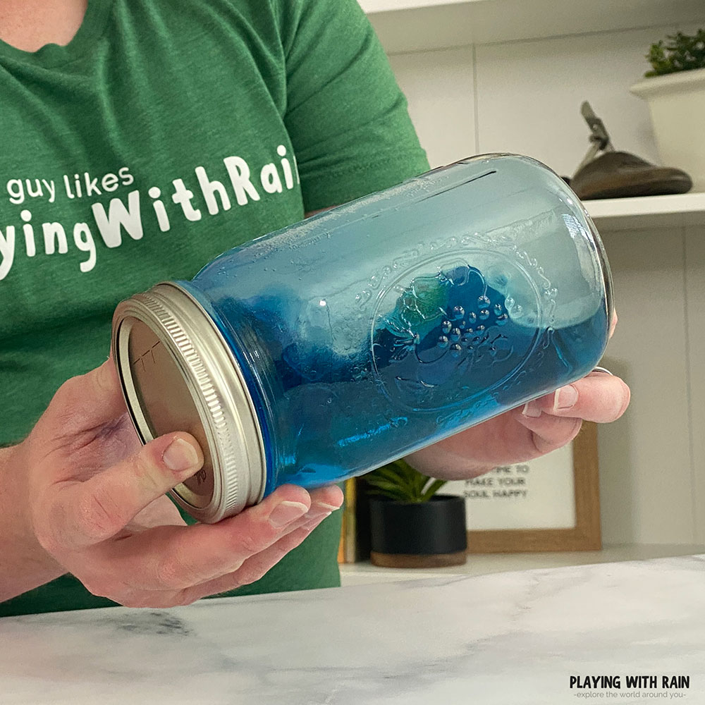 Blue water and oil splash together in a jar